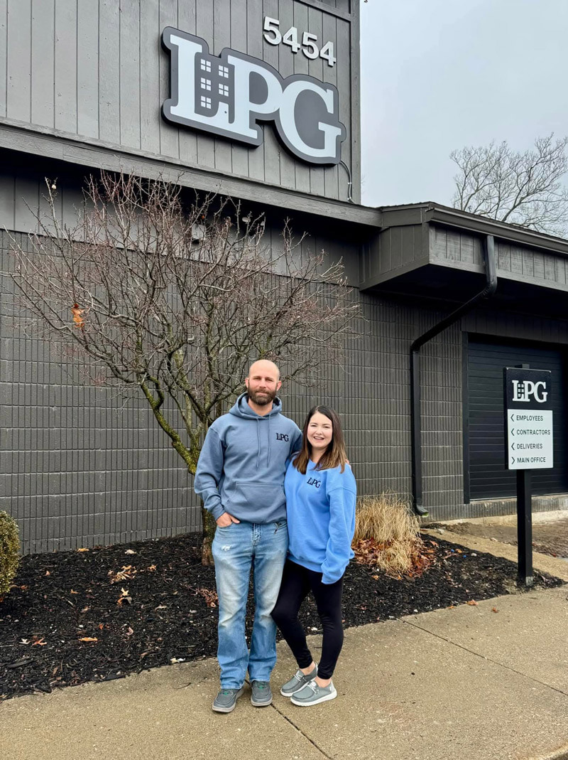 Two people pose for a picture in front of a building