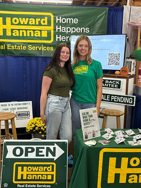 Two women pose for a picture in a Howard Hanna Real Estate booth