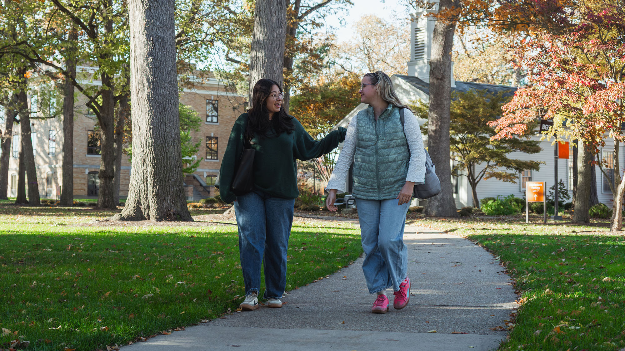 two girls walking on a sidewalk through campus
