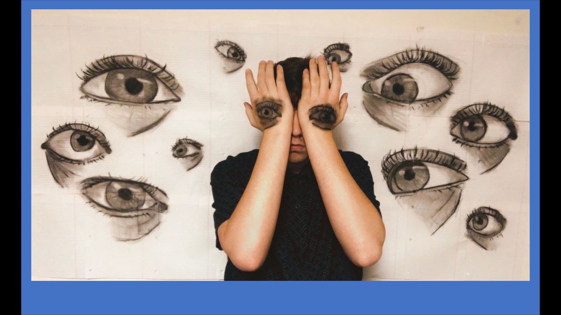 photo of large drawn eyes as a crowd looking at person posing in front with hands over face and more eyes drawn on back of hands